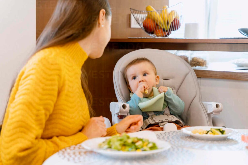 madre mirando a su bebe comiendo alimentos solidos en la trona